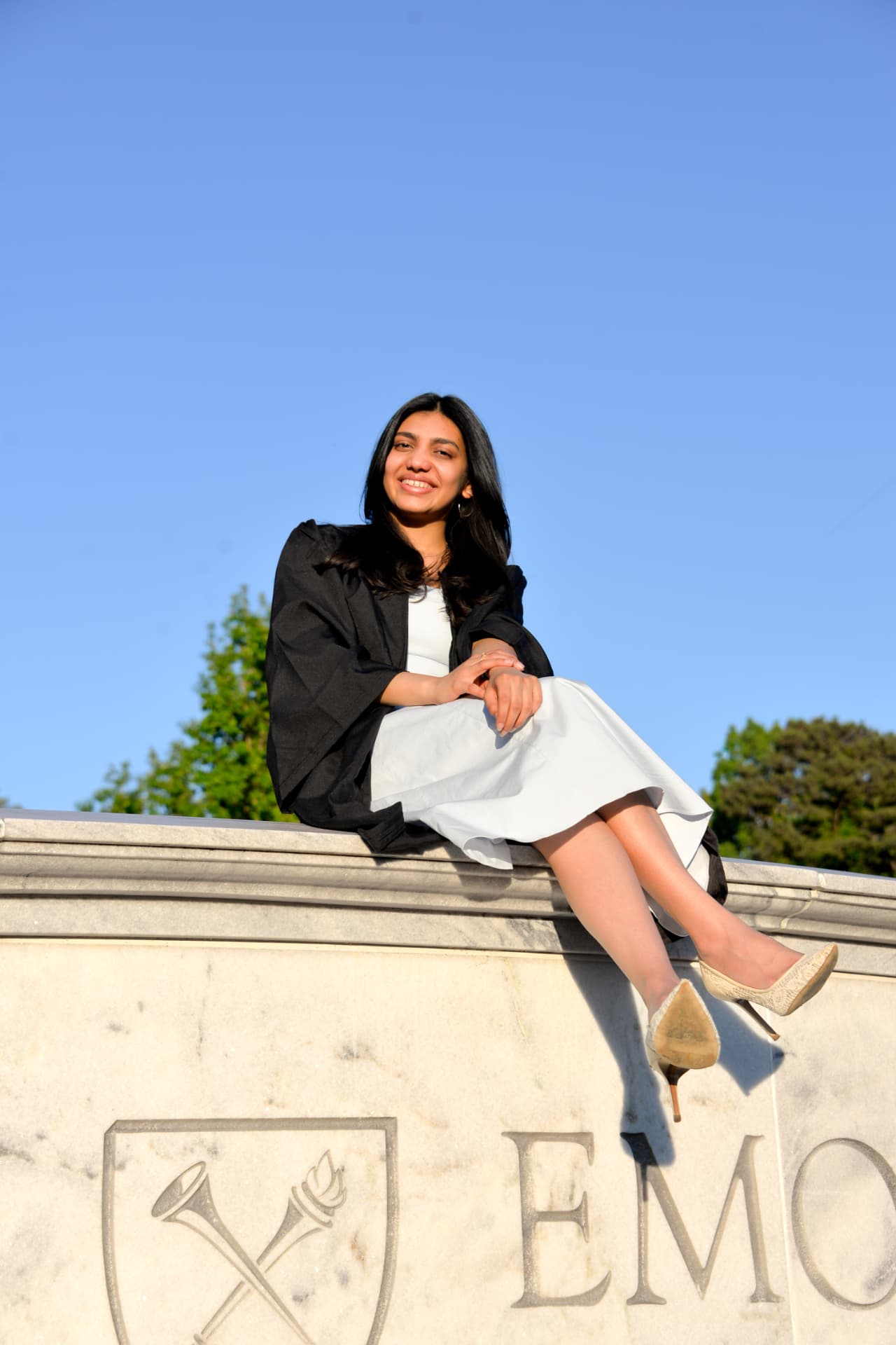 Anushka sitting on the Emory University wall in her graduation gown
